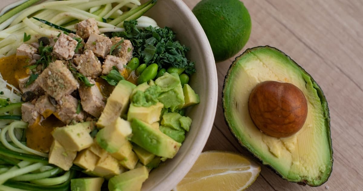 A bowl with avocado, vegetables, tofu, and a halved avocado